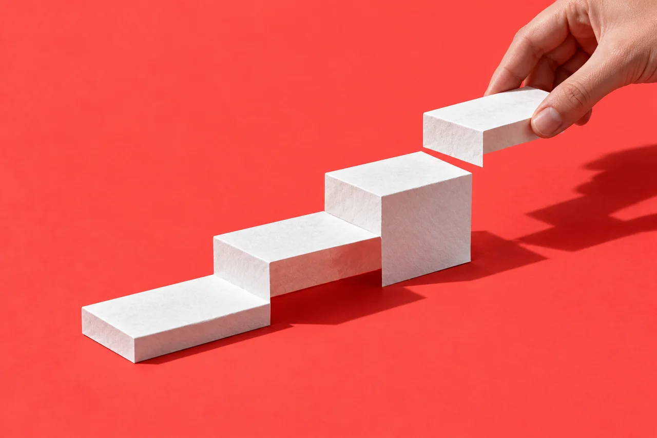 A hand places the next white block onto a sequence of steps on a coral surface.